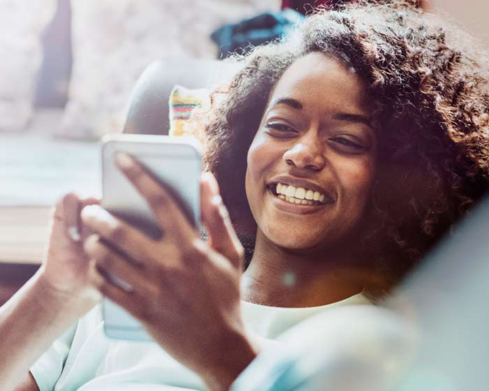 Happy woman using mobile phone on sofa